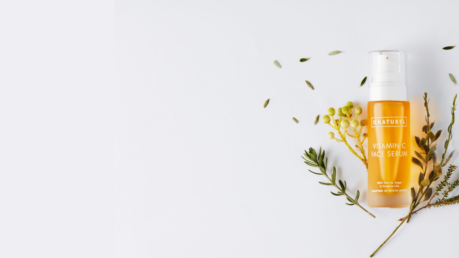 Skincare serum bottle with green leaves on a light background