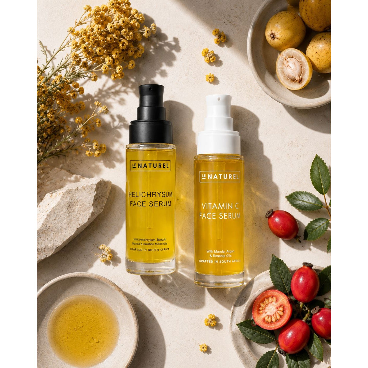 Two Le Naturel face serum bottles, Vitamin C and Helichrysum, on a textured surface with natural elements