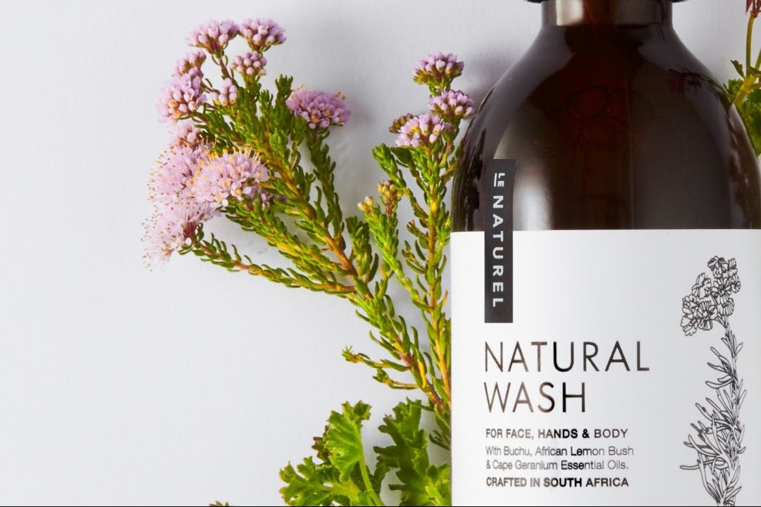 Brown bottle of natural wash with black pump and white label featuring botanical illustrations on a light gray background with green leaves and pink flowers.