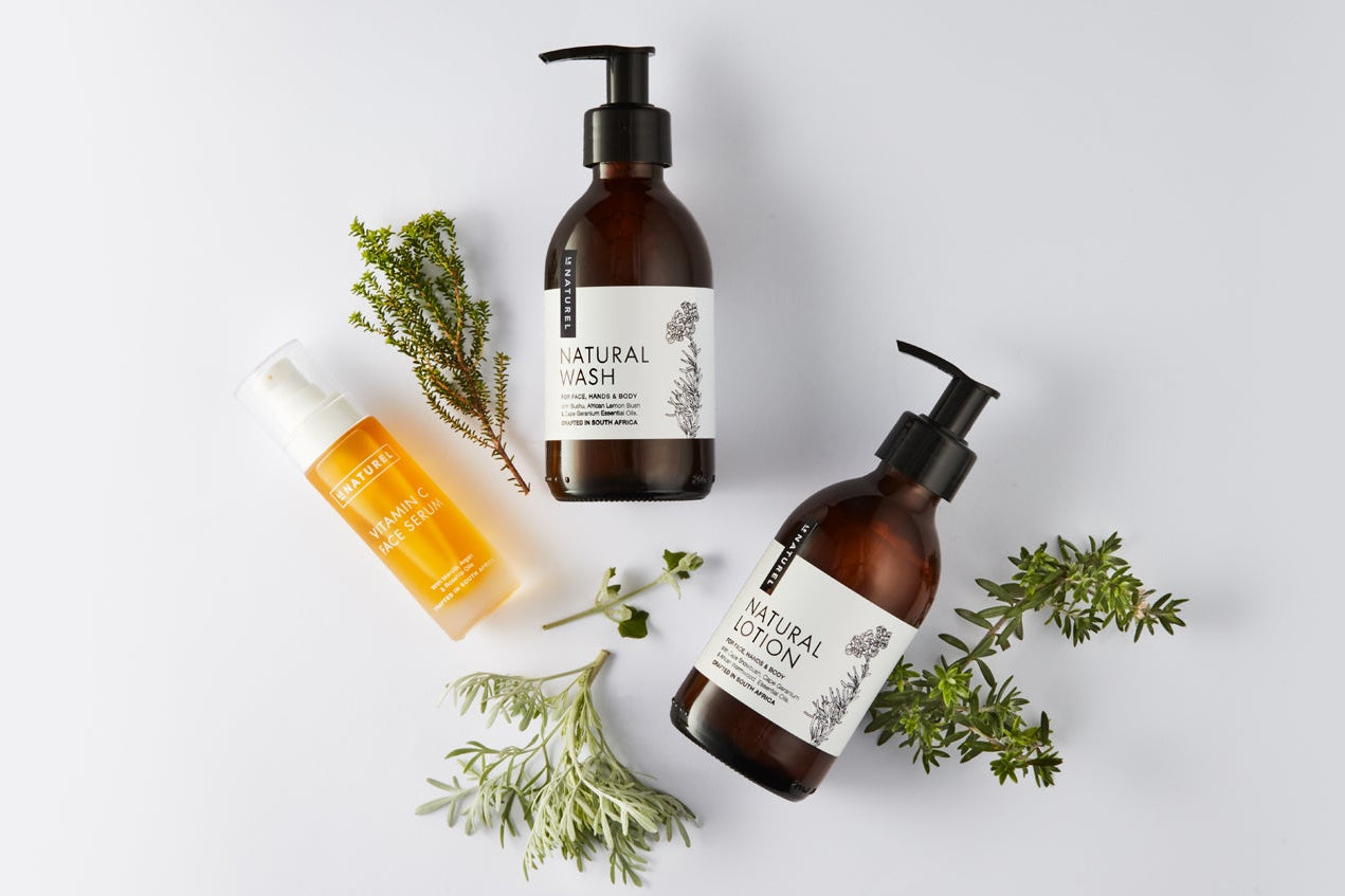 Three bottles of natural skincare products with green leaves on a light gray background